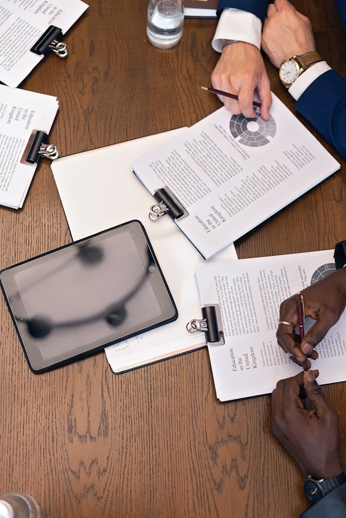 Top view of a business meeting with hands, tablets, and documents on a table.